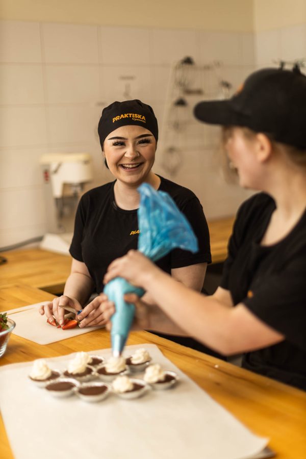 Två elever på bageri och konditori dekorerar muffins med grädde och jordgubbar.