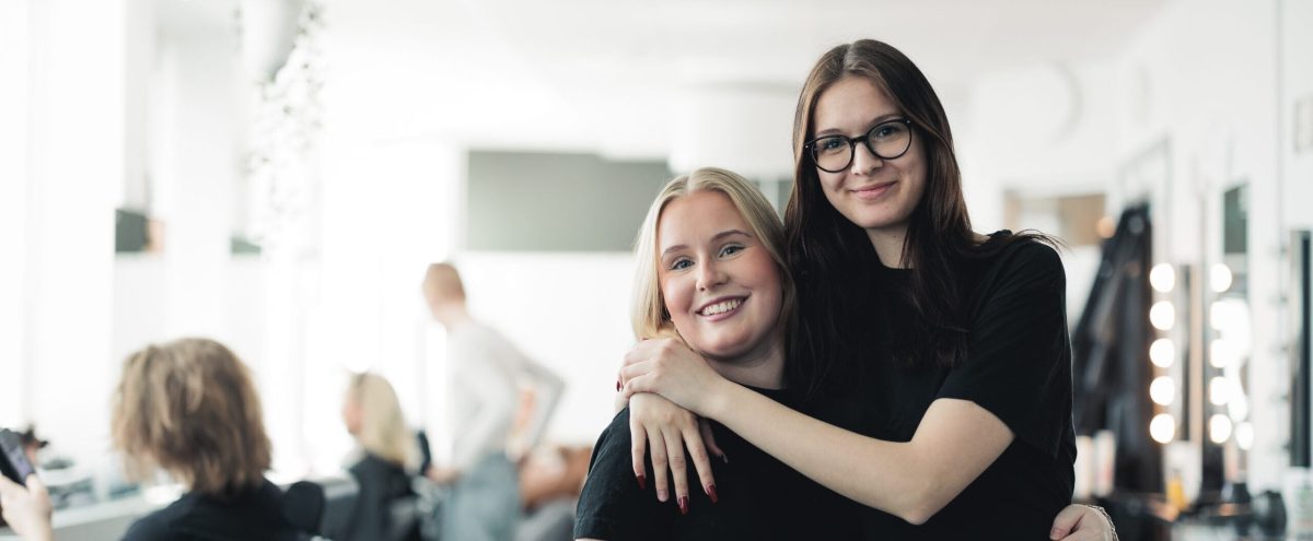 Två elever i ett klassrum håller om varandra och kollar in i kameran
