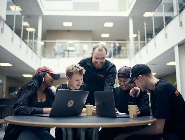 Fyra elever på Praktiska Gymnasiet som studerar och får hjälp av en lärare.