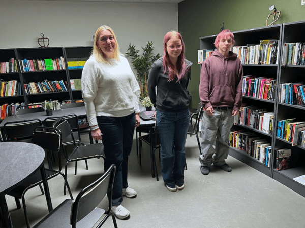 Två elever och en lärare som står i ett skolbibliotek.