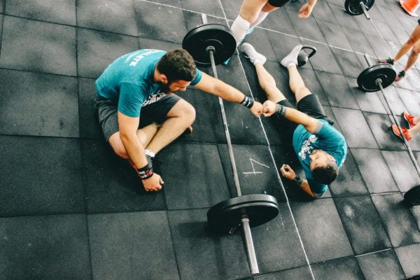 Två killar har en skivstång mellan sig och gör en "fist bump" på ett gym.