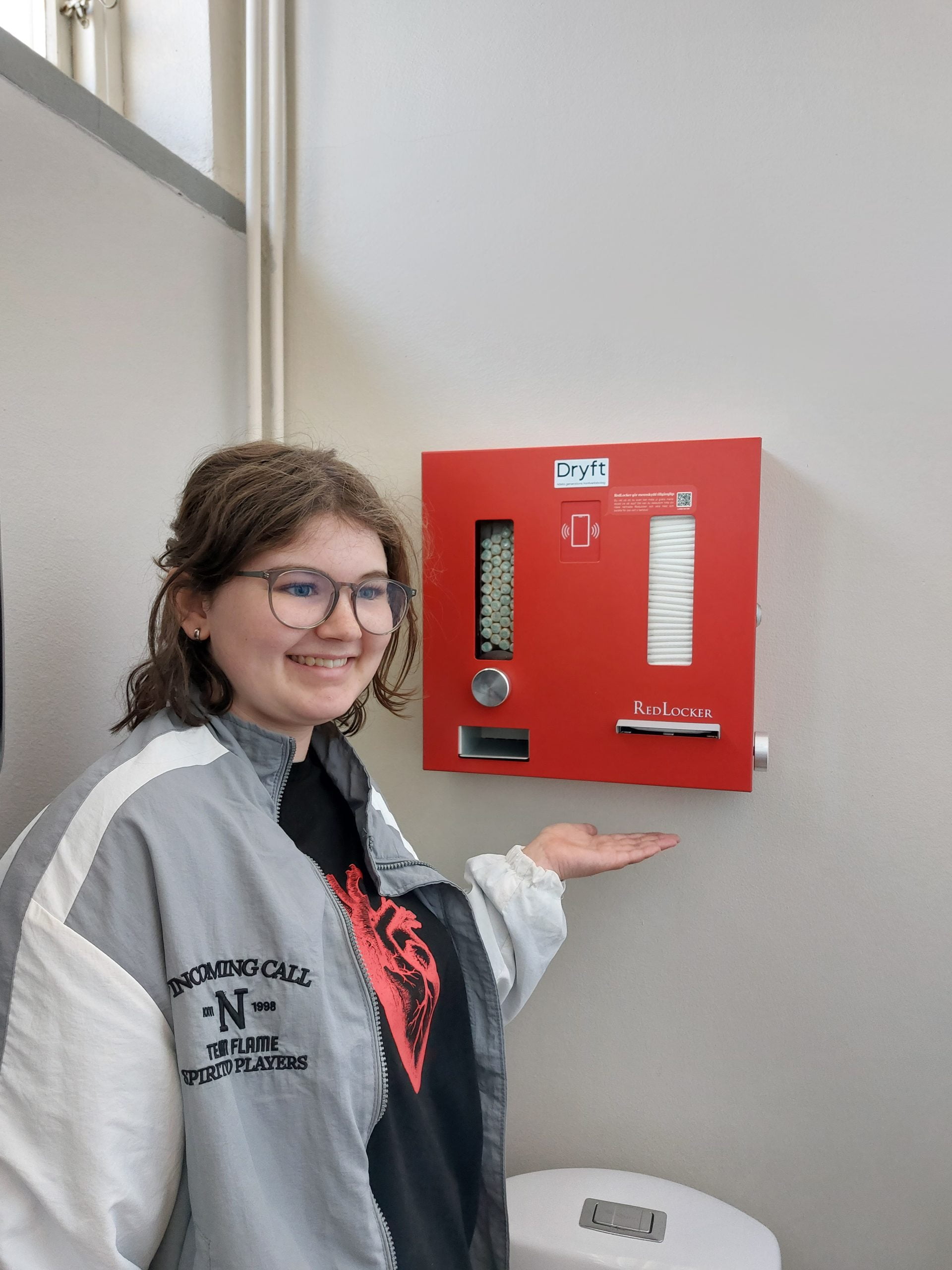 Elev står i omklädningsrummet framför en box med gratis mensskydd