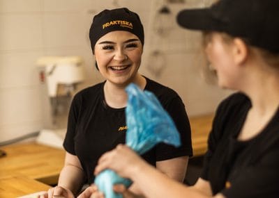 Två elever skrattar och arbetar i köket
