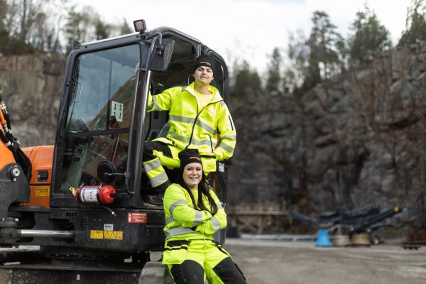 Två elever på Anläggningsfordon står vid en grävmaskin.