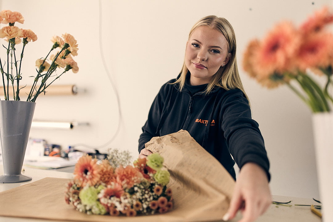 Elev som läser florist som står och slår in en bukett blommor