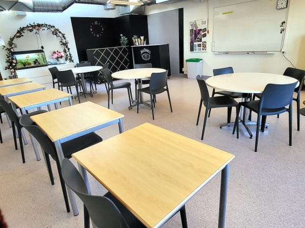 Utbildningssal med bord, stolar och en whiteboard-tavla.