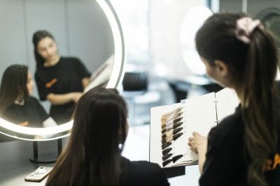 Två elever på Frisör tittar på färgprover för hårfärg.