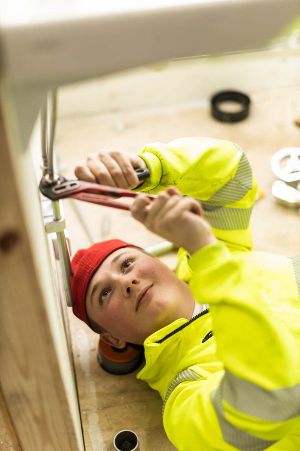Elev på VVS ligger på golvet och arbetar med rör under ett handfat.