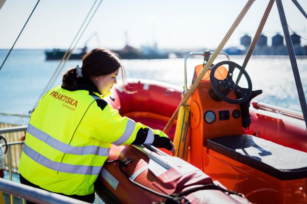 Elev på Sjöfartsutbildningen sträcker sig in i en röd räddningsbåt.