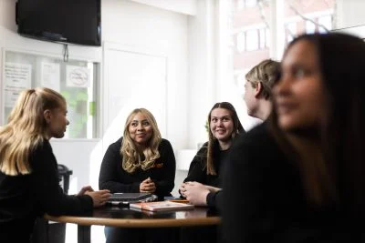 Flera elever sitter runt ett bord i skolans lokaler och pratar med varandra om tips inför öppet hus.