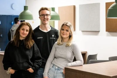 Tre elever i en skolkorridor kollar in i kameran