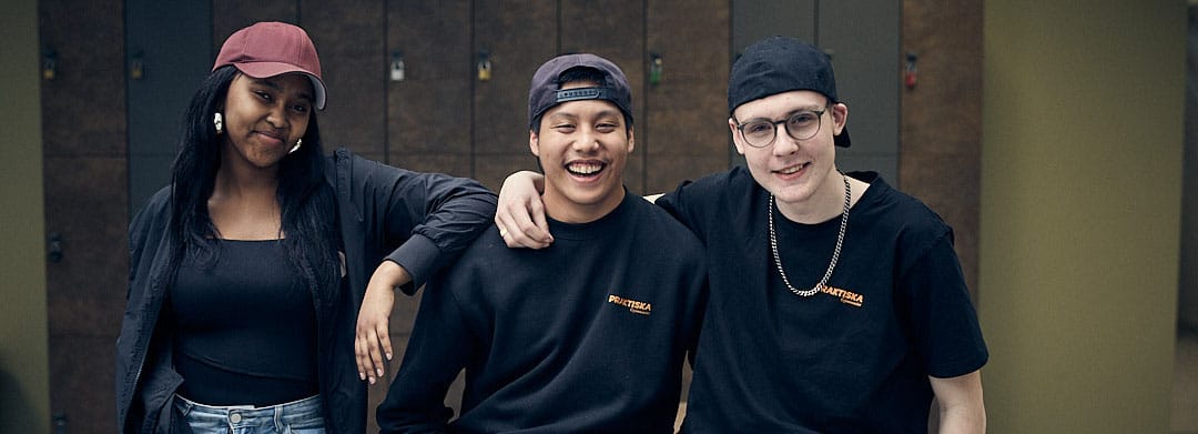 Tre elever som håller om varandra och ler till kameran.