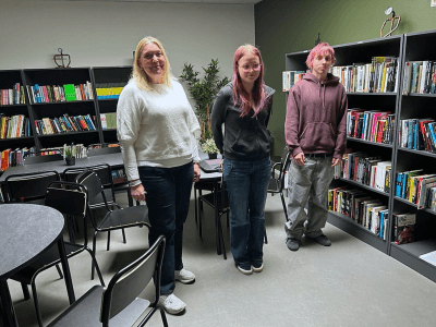 Två elever och en lärare som står i ett skolbibliotek.