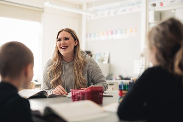 Skrattande elev som sitter och målar med två barn.