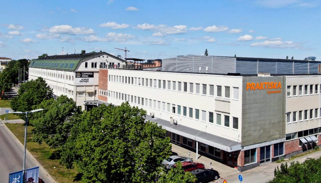 Ett fotografi på en vit byggnad med Praktiska Gymnasiets logga på fasaden.
