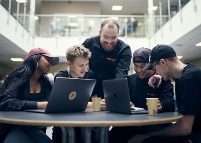 Flera elever och en lärare som diskuterar i skolans lokaler