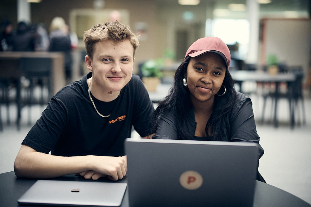 Två elever på Praktiska som sitter vid datorn och tittar in i kameran.