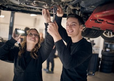 Två elever som står under en bil och arbetar