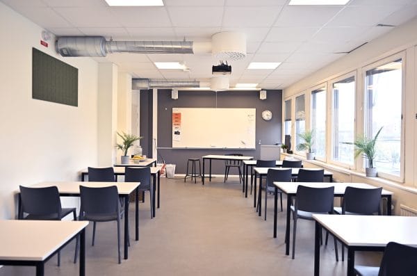 En utbildningssal med e whiteboard-tavla samt bord och stolar.