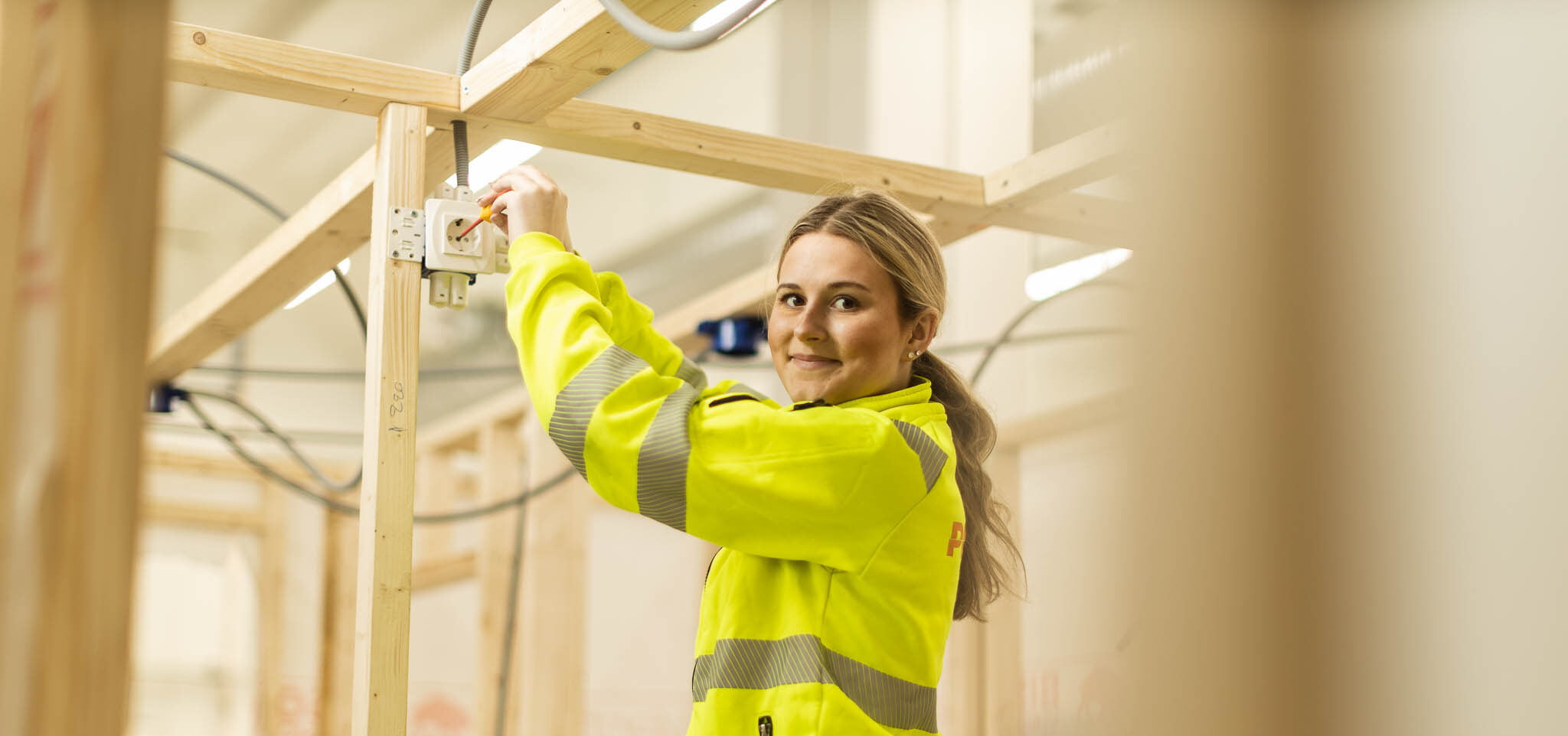 Elev i arbetskläder som studerar elteknik drar elkablar i en vägg.