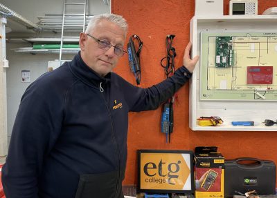 En man i en el- och energi yrekssal. På bordet finns en skylt där det står "etg college".