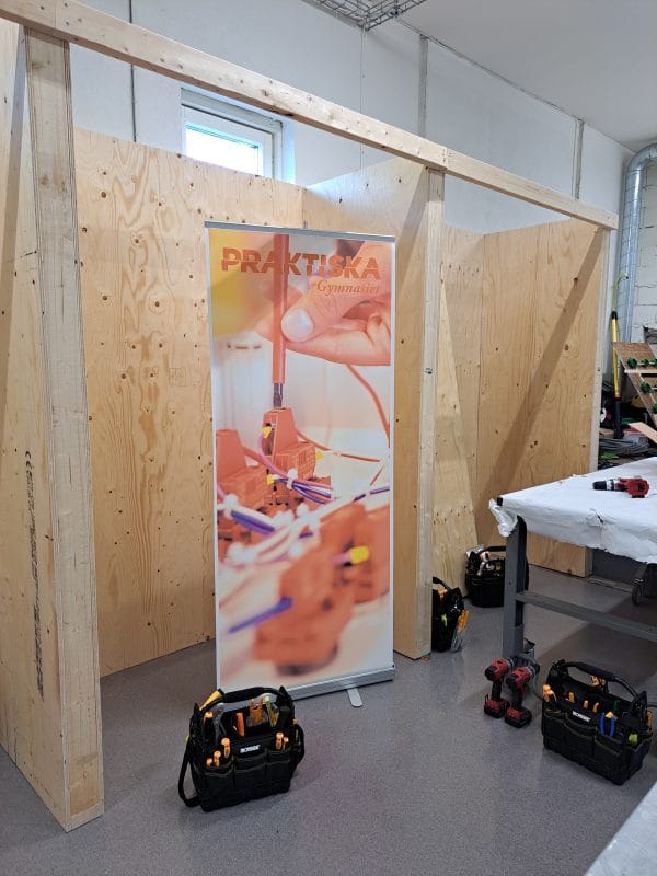 En snickarverkstad med en rollup där det står "Praktiska Gymnasiet".