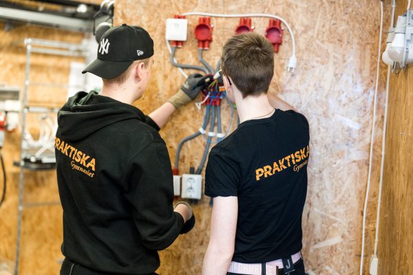 Två elever från elteknik står och installerar ett elsystem på en vägg.